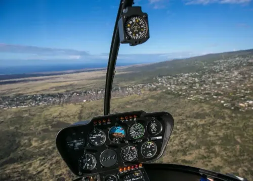 لوحة تحكم مروحية مع مؤشرات الطيران، تظهر مشهدًا واسعًا للمناظر الطبيعية تحتها، تعكس أهمية السلامة في رحلات الطيران السياحية.