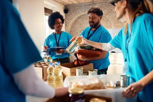 مجموعة من المتطوعين يرتدون قمصان زرقاء، يقومون بتوزيع المواد الغذائية في مركز مجتمعي، مع تفاعل إيجابي بينهم.