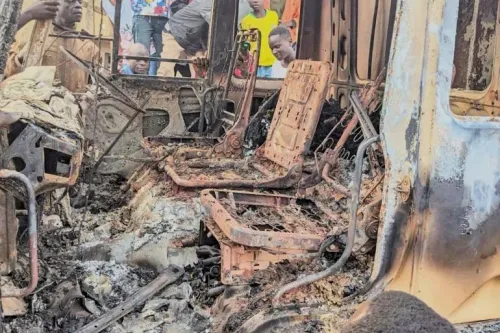 داخل حافلة محترقة تظهر مقاعد متفحمة، مع وجود أشخاص يراقبون الحطام، مما يعكس آثار الهجوم الدامي في الكونغو.