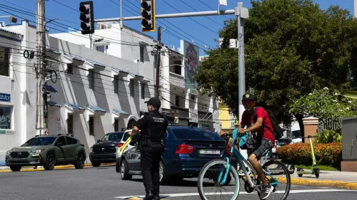 شرطي ينظم حركة المرور في تقاطع مزدحم في سان خوان، بورتوريكو، بينما يسير أحد راكبي الدراجات بجانب السيارات المتوقفة.