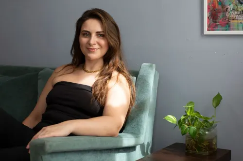 شابّة تجلس على أريكة خضراء، تبدو واثقة ومبتسمة، مع نباتات حولها، تعكس رحلة كاتي كوريو في استئصال غرسات الثدي.