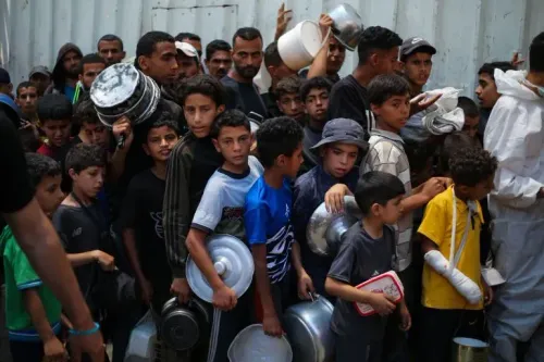 أطفال فلسطينيون يتجمعون في طابور للحصول على الطعام، مع وجود بالغين في الخلفية، في سياق الأزمة الإنسانية المستمرة في غزة.