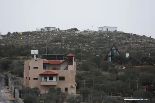 منازل تقع في منطقة جبلية بالضفة الغربية، تعكس التوترات حول الاستيطان الإسرائيلي وقرارات الحكومة بشأن تسجيل الأراضي كأملاك دولة.