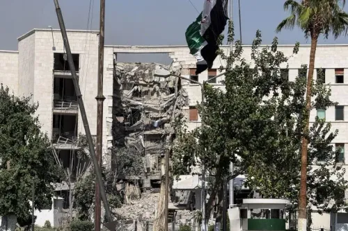 دمار كبير في مبنى في دمشق بعد الضربات الجوية الإسرائيلية، مع ظهور أعلام بين الأشجار، مما يعكس تصاعد التوترات في المنطقة.