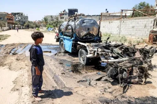 طفل يقف أمام عربة مدمرة في غزة، تعكس آثار القصف المستمر والأزمة الإنسانية المتفاقمة في المنطقة.