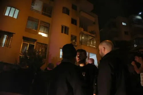 مجموعة من الأشخاص يقفون في الشارع تحت أضواء مبنى سكني في بيروت، بعد غارة جوية إسرائيلية، تعبيرًا عن القلق والخوف من التصعيد.