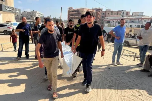 رجال يحملون جثمانًا مغطى في غزة وسط حشد من الناس، مع خلفية لمبانٍ متضررة، تعبيرًا عن الأثر المدمر للهجمات الإسرائيلية.