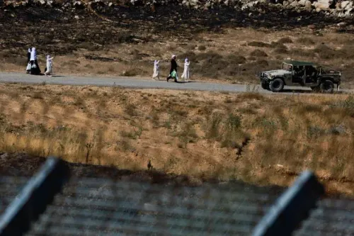 مجموعة من الأشخاص يسيرون على طريق بالقرب من مركبة عسكرية، مع خلفية من الأراضي المحترقة، في سياق التوترات العسكرية في المنطقة.