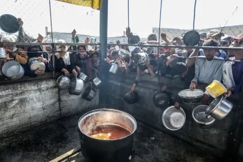 مشهد لجماهير من الفلسطينيين في غزة يتجمعون حول قدر كبير للطعام، حاملين أوعية فارغة، في سياق أزمة إنسانية متفاقمة.