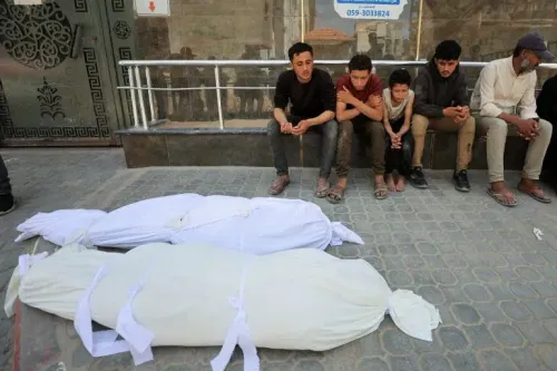 شبان يجلسون بجانب جثتين مغطاتين بأقمشة بيضاء في غزة، تعبيراً عن الحزن بعد تصعيد العنف في المنطقة.