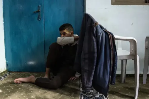 شاب فلسطيني يجلس على الأرض بجوار باب أزرق، يعبر عن الإحباط والقلق بعد اعتقاله، وسط أجواء من التوتر في طوباس.