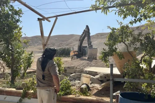 رجل فلسطيني يراقب جرافة إسرائيلية تهدم منازل في حي عين الديوك بأريحا وسط تدمير واسع للممتلكات الفلسطينية.