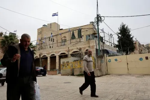 رجلان يسيران في شوارع الضفة الغربية، مع ظهور علم إسرائيل على المبنى الخلفي، في سياق التوترات المستمرة والعنف ضد الفلسطينيين.