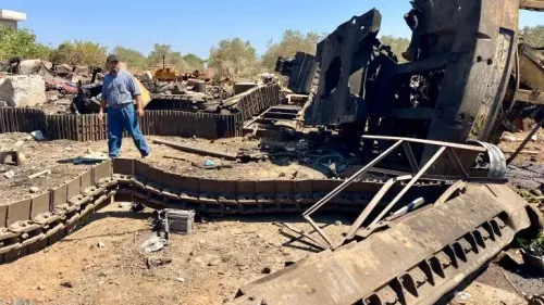 رجل يقف بين حطام دبابات مدمرة في منطقة تعرضت للدمار في جنوب لبنان، مما يعكس آثار الصراع المستمر.