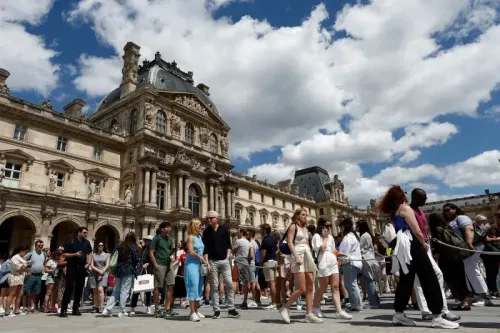 طابور طويل من الزوار أمام متحف اللوفر في باريس، تحت سماء زرقاء مع غيوم بيضاء، مما يعكس الازدحام السياحي المتزايد.