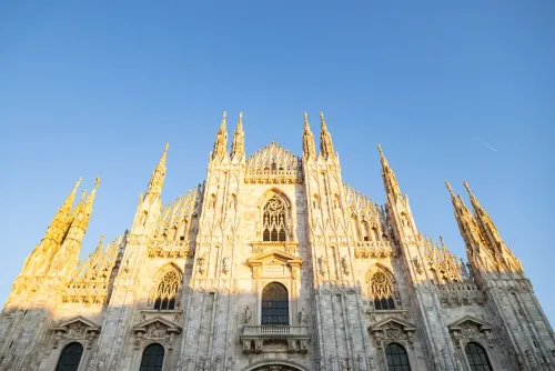 واجهة كاتدرائية ميلانو تتألق تحت أشعة الشمس، مع تفاصيل معمارية معقدة وأبراج مميزة، تعكس التراث الثقافي الإيطالي.