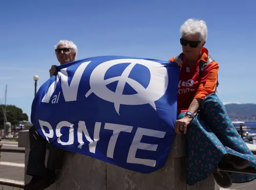 شخصان يحملان لافتة زرقاء مكتوب عليها "NO al PONTE"، تعبيرًا عن معارضتهما لبناء جسر مضيق ميسينا في إيطاليا.