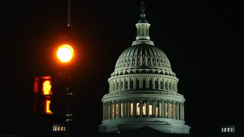مبنى الكابيتول الأمريكي مضاء في الليل، مع إشارة مرور صفراء تضيء في المقدمة، مما يعكس التوترات الاقتصادية والسياسية الحالية.