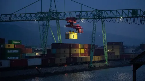 صورة لمرفأ ليلي حيث يتم رفع حاوية شحن بواسطة رافعة، مع وجود حاويات ملونة مرتبة على الرصيف، مما يعكس أهمية التجارة في الاقتصاد الألماني.