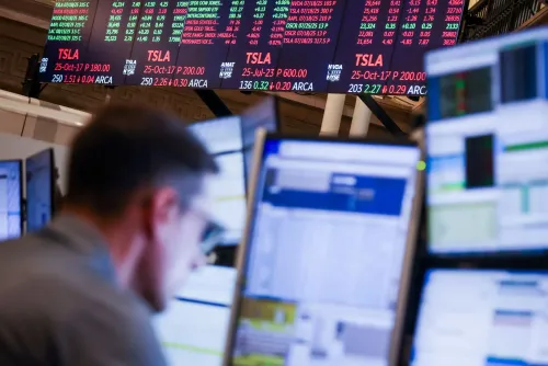 شاشة عرض تعرض أسعار أسهم تسلا (TSLA) مع بيانات السوق، بينما يظهر متداول يعمل أمام عدة شاشات في خلفية الصورة.