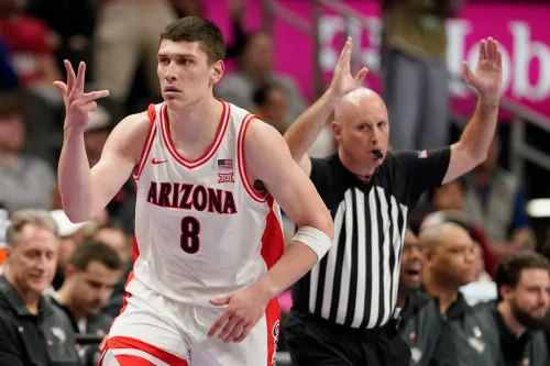 لاعب كرة سلة من فريق أريزونا يرتدي القميص رقم 8، يحتفل بعد تسجيل نقطة، بينما الحكم يشير بإشارة فنية في مباراة NCAA.