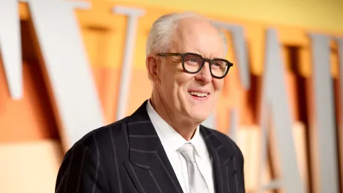 جون ليثغو مبتسم، يرتدي بدلة أنيقة مع نظارات، يتحدث عن ذكرياته في مسلسل "الصخرة الثالثة من الشمس" وتأثيره على مسيرته الفنية.