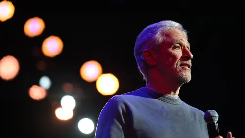 جون ستيوارت يتحدث على المسرح، مع إضاءة خلفية ملونة، معبراً عن استيائه من إلغاء برنامج ستيفن كولبرت على شبكة سي بي إس.