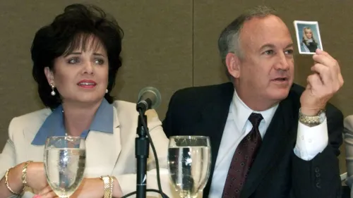 والدا جون بينيت رامزي يجلسان معًا خلال مؤتمر صحفي، حيث يُظهر والدها صورة لها، في سياق الدعوات لمواصلة التحقيق في قضيتها.