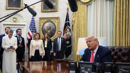 اجتماع في المكتب البيضاوي مع الرئيس ترامب، حيث يتحدث أمام مجموعة من المساعدين، مع وجود علمين أمريكيين وصورة لجورج واشنطن خلفه.