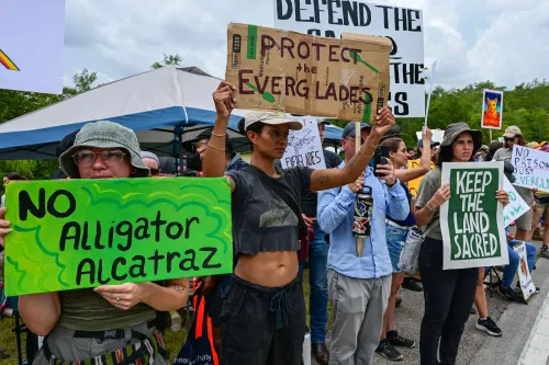 محتجون يحملون لافتات تعبر عن معارضتهم لمركز احتجاز المهاجرين في إيفرجليدز، مطالبين بحماية البيئة والأراضي المقدسة.