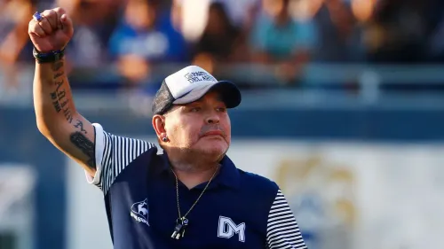 دييغو مارادونا، أسطورة كرة القدم الأرجنتيني، يرفع يده في احتفال، مع خلفية جماهيرية، بعد وفاته التي أثارت جدلاً قانونياً.