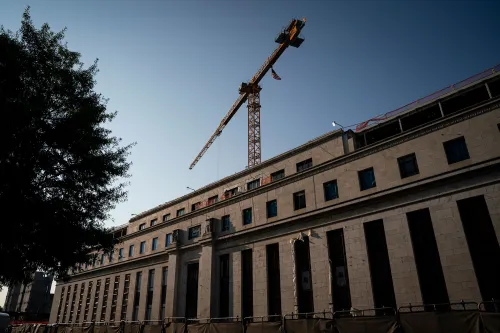 موقع بناء يتضمن رافعة عالية فوق مبنى حكومي، مع أشجار في المقدمة، يعكس التغيرات في السياسة النقدية الأمريكية.