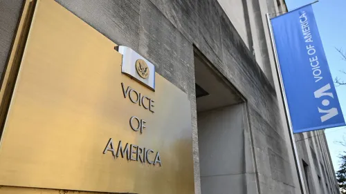 لافتة ذهبية مكتوب عليها "صوت أمريكا" مع شعار الوكالة، تظهر على مبنى إذاعة صوت أمريكا، رمزًا لحرية الصحافة.