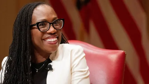 القاضية كيتانجي براون جاكسون مبتسمة أثناء حديثها، مع العلم الأمريكي خلفها، تعبر عن آرائها حول قضايا المحكمة العليا.