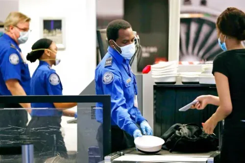 موظفان من إدارة أمن النقل (TSA) يرتديان زيًا رسميًا ويقومون بفحص الأمتعة في مطار، مع وجود مسافرة تتفاعل معهم.