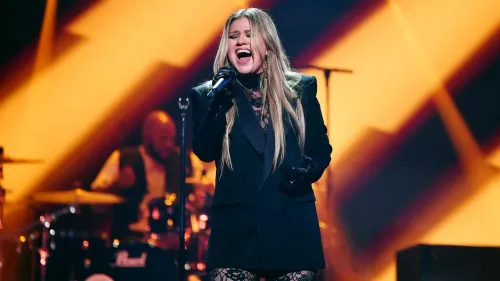 كيلي كلاركسون تؤدي على المسرح، مرتدية ملابس سوداء، مع تعبيرات وجه تعكس مشاعرها بعد تأجيل عرضها في لاس فيغاس.