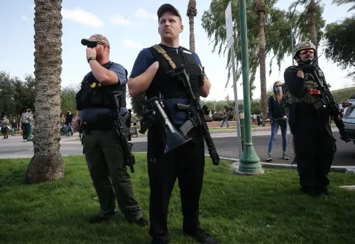 مجموعة من المتظاهرين المسلحين في منطقة عامة، حيث يحملون أسلحة نارية، مع وجود أشخاص آخرين في الخلفية، مما يعكس التوترات حول حقوق حمل السلاح.