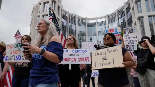 محتجون يحملون لافتات تدعو لإنهاء مداهمات الهجرة، مع التركيز على حقوق الإنسان والعدالة، أمام مبنى حكومي.