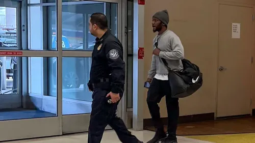 مواطن أمريكي يخرج من المطار برفقة ضابط، بعد الإفراج عنه من السجون الكويتية، في خطوة تعكس العلاقات الأمريكية الكويتية.