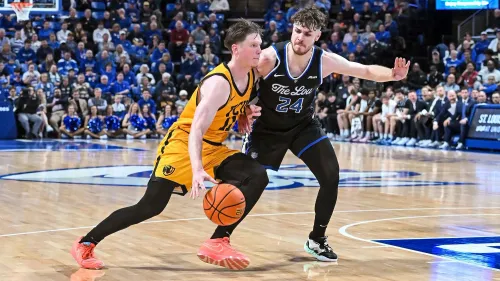 لاعبان يتنافسان على الكرة في مباراة كرة سلة جامعية بين جامعة فرجينيا كومنولث وفريق سانت لويس، مع جمهور متحمس في الخلفية.