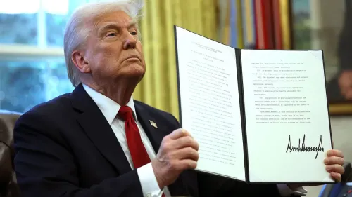 دونالد ترامب يحمل أمرًا تنفيذيًا في المكتب البيضاوي، مع تعبير جاد على وجهه، وسط أجواء رسمية.