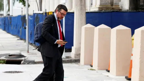 ستانلي وودوارد، محامي ترامب، يسير في الشارع مرتديًا بدلة رسمية ويحمل هاتفه، مع وجود حواجز في الخلفية.