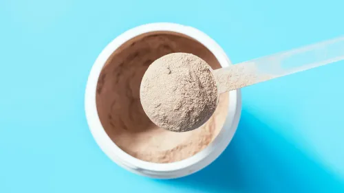 مسحوق بروتين بلون بني فاتح في ملعقة بلاستيكية، بجانب علبة بيضاء، على خلفية زرقاء، يشير إلى مستويات المعادن الثقيلة في المنتجات.