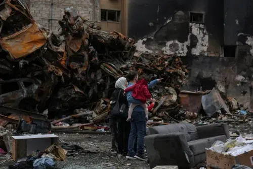 عائلة تتفقد الأضرار في منطقة مدمرة، حيث تظهر السيارات المحترقة والخراب، في سياق التوترات المستمرة بين لبنان وإسرائيل.