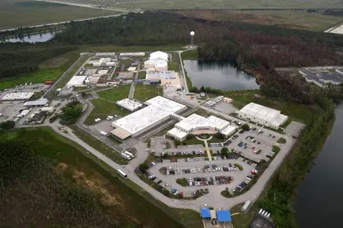 صورة جوية لمركز احتجاز للمهاجرين في فلوريدا، تُظهر المباني المحاطة بالمساحات الخضراء والمياه، تعكس ظروف الاحتجاز القاسية والاكتظاظ.