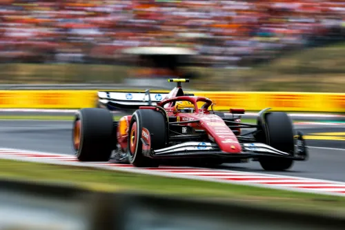 سيارة فيراري تسير بسرعة عالية على حلبة سباق الجائزة الكبرى المجري، مع خلفية جماهيرية ملونة، تعكس تحديات لويس هاميلتون في السباق.