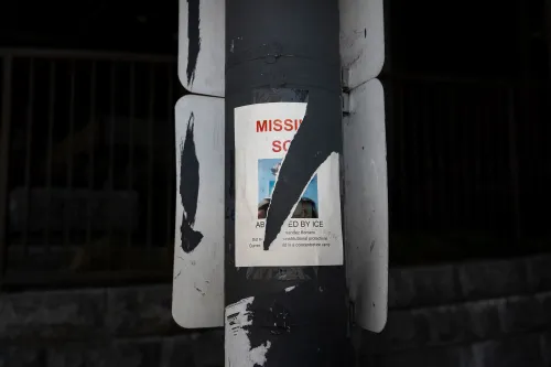 ملصق مفقود على عمود، يحمل صورة شخص مفقود يُعتقد أنه تم احتجازه من قبل إدارة الهجرة والجمارك، مع تفاصيل الاتصال.