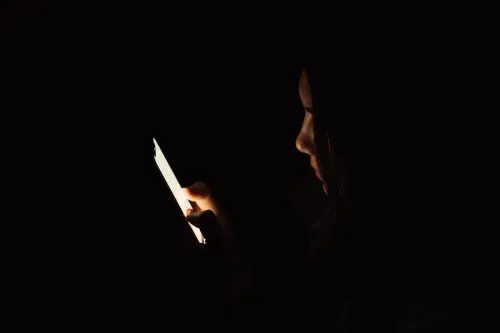امرأة في الظلام تركز على شاشة هاتفها الذكي، تعكس تجربة الوحدة والتواصل الاجتماعي في العصر الرقمي.