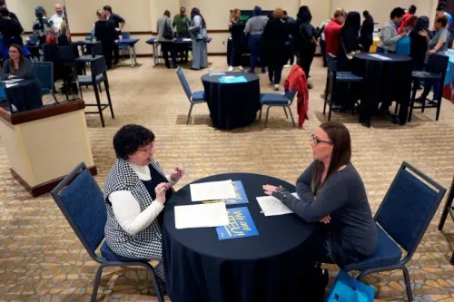 امرأتان تجلسان على طاولة في حدث توظيف، حيث يتحدثن عن فرص العمل وسط مجموعة من المشاركين في الخلفية.