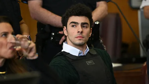 لويجي مانجيوني، المتهم بقتل الرئيس التنفيذي لشركة UnitedHealthcare، يجلس في قاعة المحكمة مرتديًا سترة واقية، مع محاميه في الخلفية.